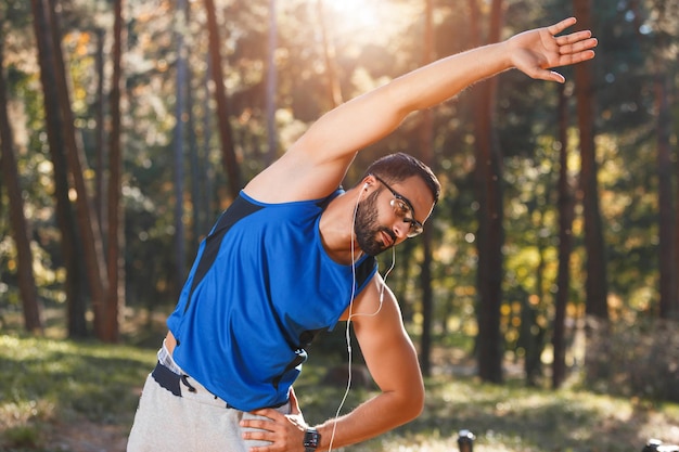 Jovem homem barbudo multicultural atlético usando óculos esportivos ouvindo sua música favorita enquanto fazia seu estilo de vida saudável de exercício matinal e conceito de pessoas