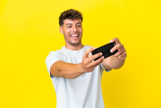 Jovem homem bonito caucasiano isolado em fundo amarelo brincando com o celular