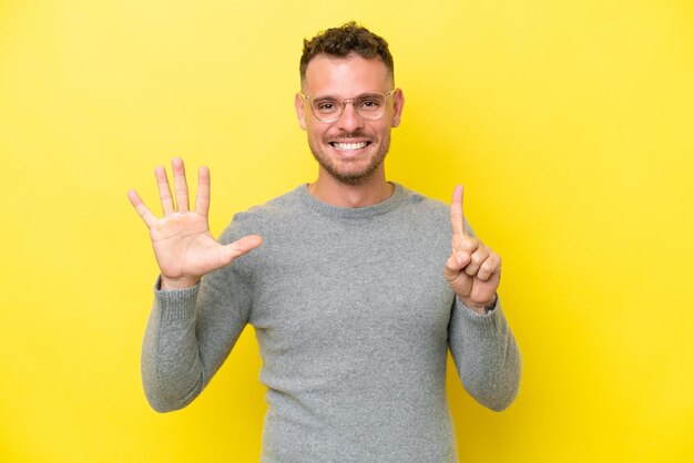 Jovem homem bonito caucasiano isolado em fundo amarelo contando seis com os dedos