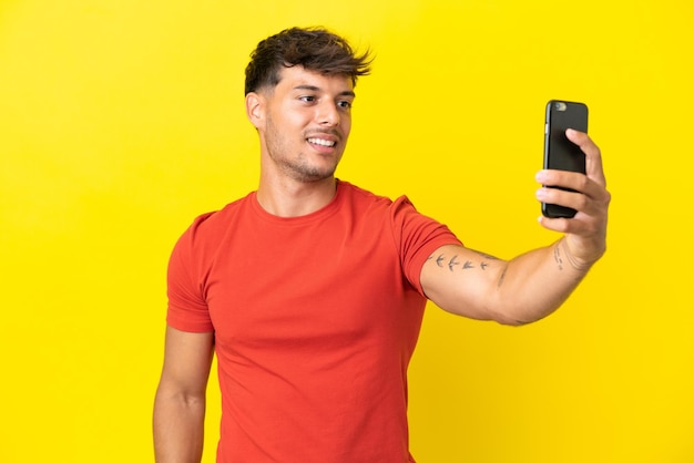 Jovem homem bonito caucasiano isolado em fundo amarelo fazendo uma selfie