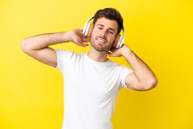 Jovem homem bonito, caucasiano, isolado em um fundo amarelo ouvindo música