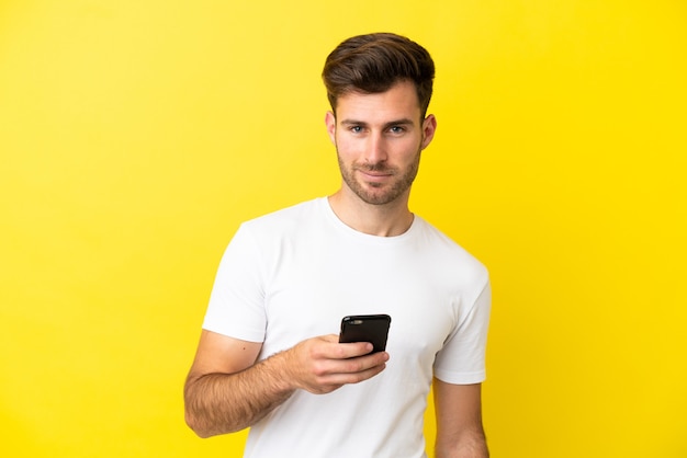 Jovem homem bonito, caucasiano, isolado em um fundo amarelo, usando telefone celular