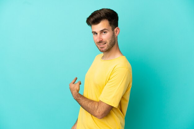 Jovem homem bonito, caucasiano, isolado em um fundo azul, apontando para trás