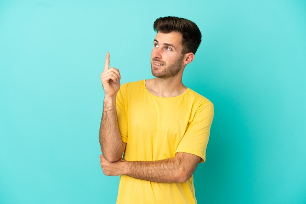 Jovem homem bonito, caucasiano, isolado em um fundo azul apontando para uma ótima ideia