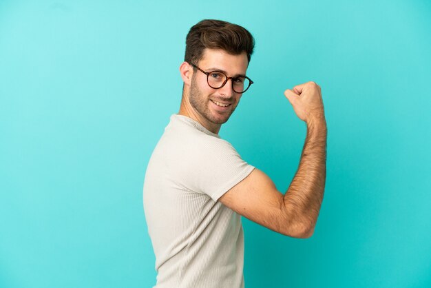 Jovem homem bonito caucasiano isolado em um fundo azul fazendo um gesto forte