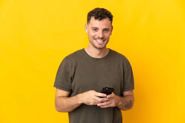 Jovem homem bonito, caucasiano, isolado na parede amarela, enviando uma mensagem com o celular