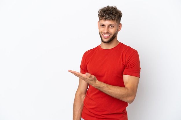 Jovem homem bonito, caucasiano, isolado no fundo branco, apresentando uma ideia enquanto olha, sorrindo para