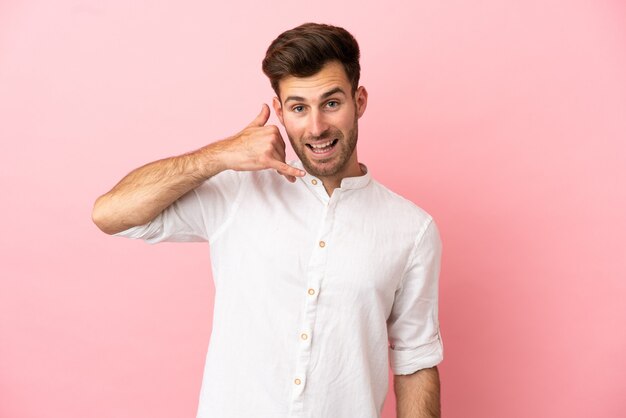 Jovem homem bonito caucasiano isolado no fundo rosa, fazendo gesto de telefone. Ligue-me de volta sinal