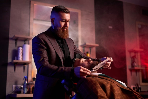 Jovem homem bonito, caucasiano, na cadeira do barbeiro, fazendo o procedimento de barbear