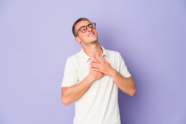 Jovem homem bonito caucasiano rindo mantendo as mãos no coração, o conceito de felicidade.