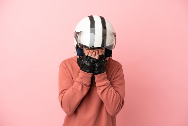 Jovem homem branco avermelhado com capacete de motociclista isolado em um fundo rosa com expressão cansada e doente