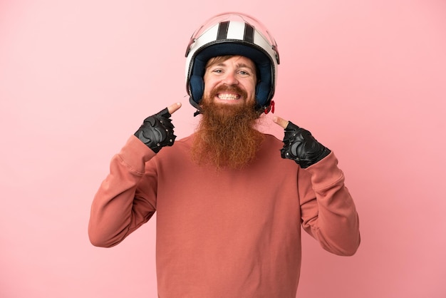 Jovem homem branco avermelhado com um capacete de motociclista isolado em um fundo rosa fazendo um gesto de polegar para cima