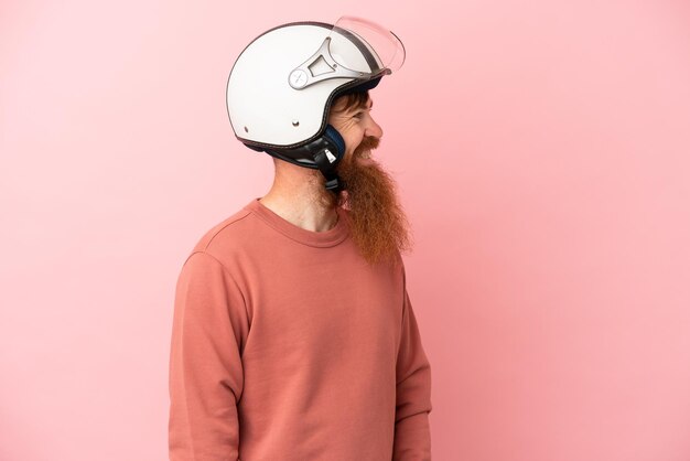 Jovem homem branco avermelhado com um capacete de motociclista isolado em um fundo rosa olhando de lado