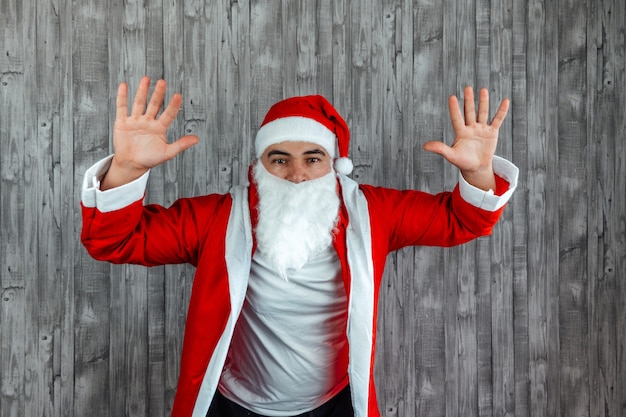 Jovem homem branco vestido de Papai Noel com as mãos para cima