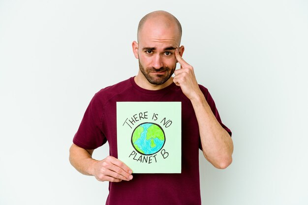 Jovem homem careca caucasiano segurando um cartaz de não há planeta B isolado na parede roxa, mostrando um gesto de decepção com o dedo indicador.