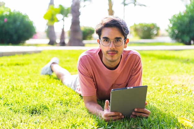 Jovem homem caucasiano ao ar livre em um parque segurando um tablet