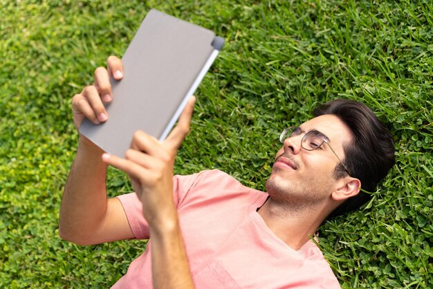 Jovem homem caucasiano ao ar livre em um parque segurando um tablet