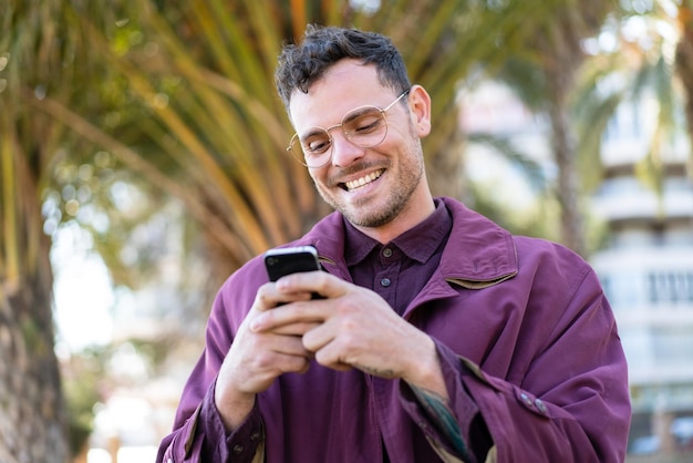 Jovem homem caucasiano ao ar livre enviando uma mensagem ou e-mail com o celular