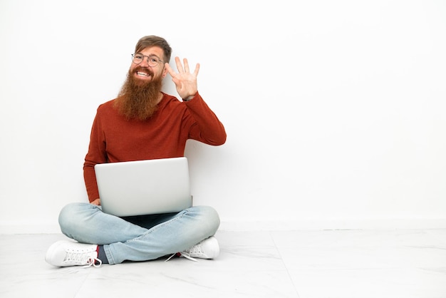 Jovem homem caucasiano avermelhado com laptop isolado em fundo branco feliz e contando quatro com os dedos