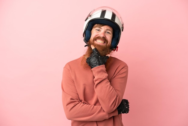 Jovem homem caucasiano avermelhado com um capacete de moto isolado em fundo rosa feliz e sorridente
