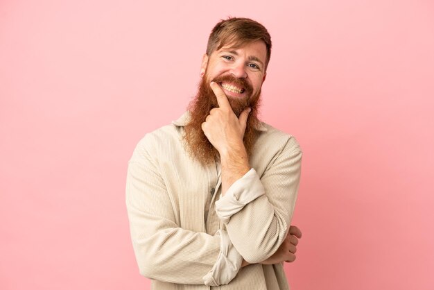 Jovem homem caucasiano avermelhado isolado em fundo rosa feliz e sorridente