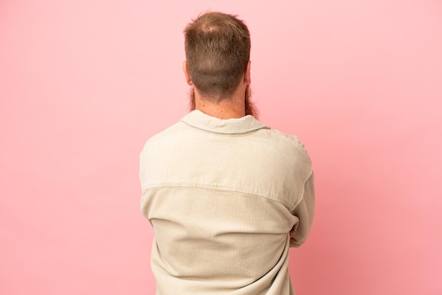 Jovem homem caucasiano avermelhado isolado em fundo rosa na posição traseira