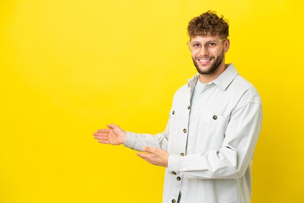 Jovem homem caucasiano bonito isolado em fundo amarelo, estendendo as mãos para o lado para convidar para vir