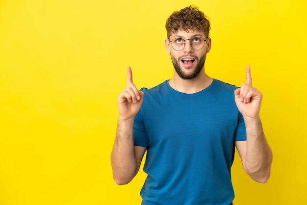 Jovem homem caucasiano bonito isolado em fundo amarelo surpreso e apontando para cima