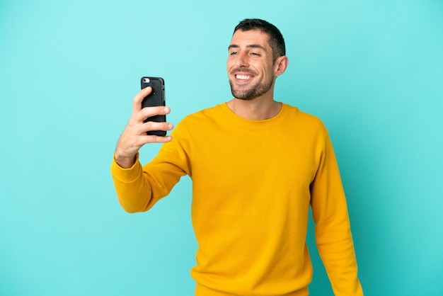 Jovem homem caucasiano bonito isolado em fundo azul fazendo uma selfie