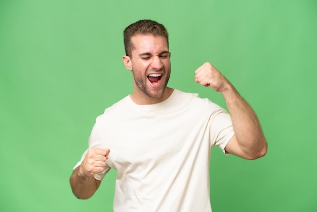Jovem homem caucasiano bonito isolado em fundo de croma verde celebrando uma vitória