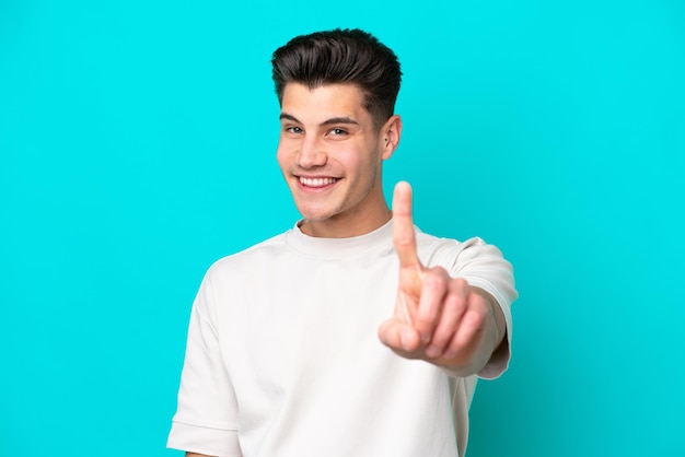 Jovem homem caucasiano bonito isolado no fundo azul mostrando e levantando um dedo