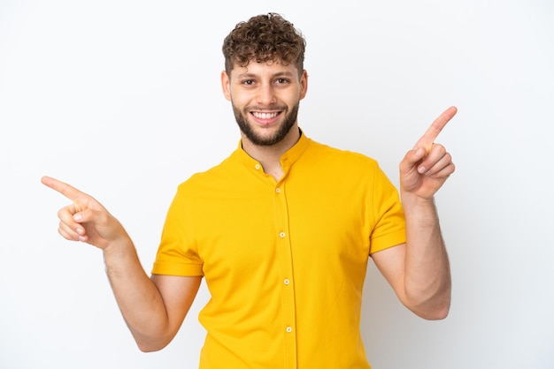 Jovem homem caucasiano bonito isolado no fundo branco apontando o dedo para as laterais e feliz