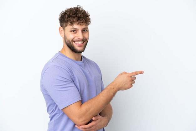 Jovem homem caucasiano bonito isolado no fundo branco, apontando o dedo para o lado