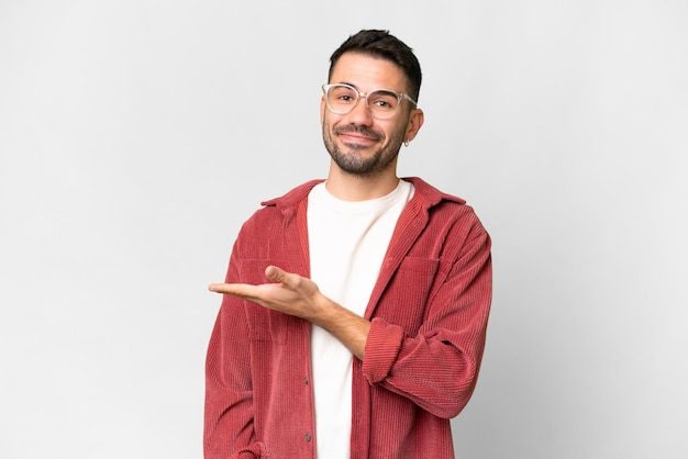 Jovem homem caucasiano bonito sobre fundo branco isolado apresentando uma ideia enquanto olha sorrindo para