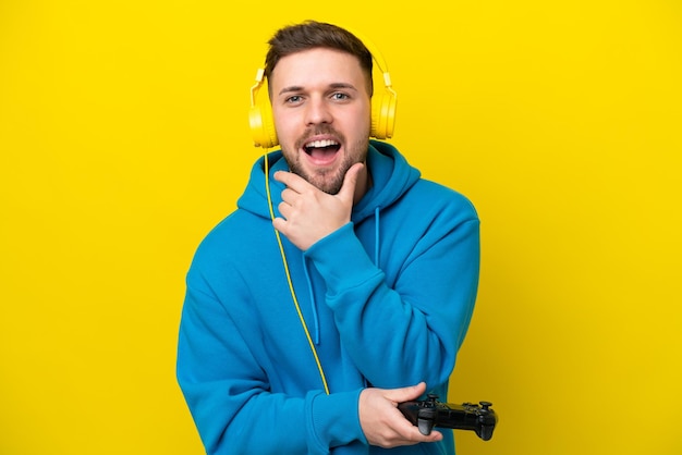 Jovem homem caucasiano brincando com um controlador de videogame isolado em fundo amarelo feliz e sorridente