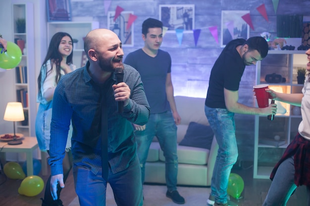 Foto jovem homem caucasiano cantando no microfone para o entretenimento de seus amigos na festa.