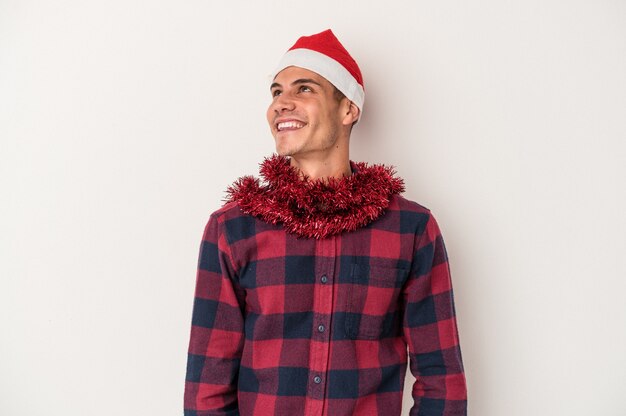 Foto jovem homem caucasiano celebrando o natal isolado no fundo branco, sonhando em alcançar objetivos e propósitos