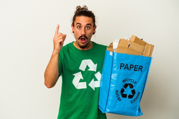 Jovem homem caucasiano com cabelo comprido, reciclando papelão isolado no fundo branco, tendo uma ideia, o conceito de inspiração.