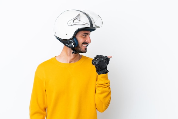 Jovem homem caucasiano com capacete de moto isolado no fundo branco, apontando para o lado para apresentar um produto