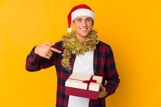 Jovem homem caucasiano com chapéu de natal segurando um presente isolado em amarelo unhas roendo, nervoso e muito ansioso.