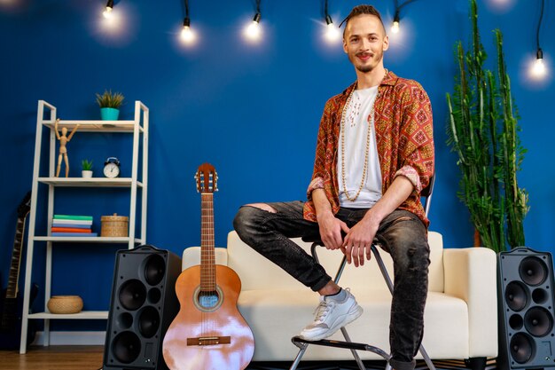 Jovem homem caucasiano com dreadlocks, sentado no sofá na sala de estar perto de guitarra