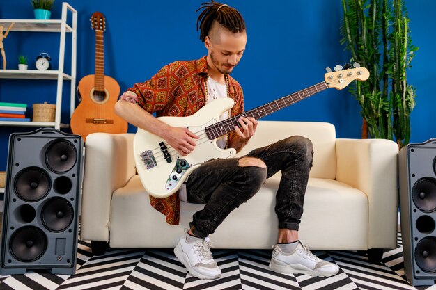 Jovem homem caucasiano com dreadlocks tocando guitarra no quarto dele