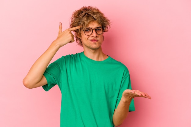 Jovem homem caucasiano com maquiagem isolada no fundo rosa, segurando e mostrando um produto por lado.