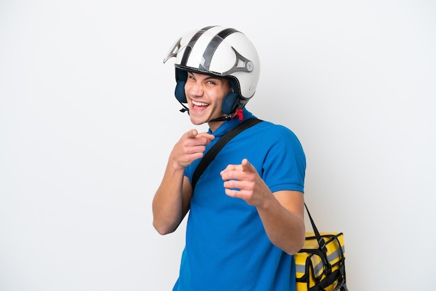 Jovem homem caucasiano com mochila térmica isolada no fundo branco, apontando para a frente e sorrindo