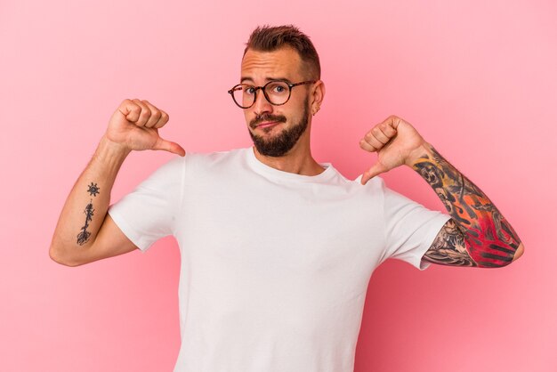 Jovem homem caucasiano com tatuagens isoladas em um fundo rosa se sente orgulhoso e autoconfiante, exemplo a seguir.