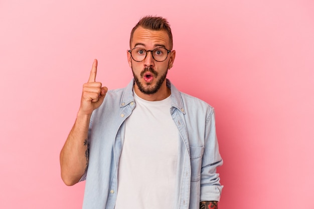 Jovem homem caucasiano com tatuagens isoladas em um fundo rosa, tendo uma ideia, o conceito de inspiração.