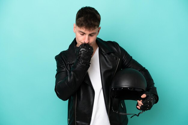 Jovem homem caucasiano com um capacete de moto isolado em fundo azul com dúvidas
