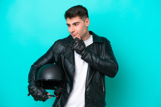 Jovem homem caucasiano com um capacete de moto isolado em fundo azul, olhando para o lado e sorrindo