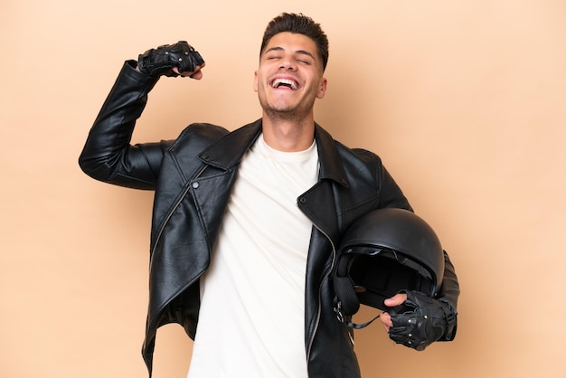 Foto jovem homem caucasiano com um capacete de moto isolado em fundo bege, fazendo um gesto forte