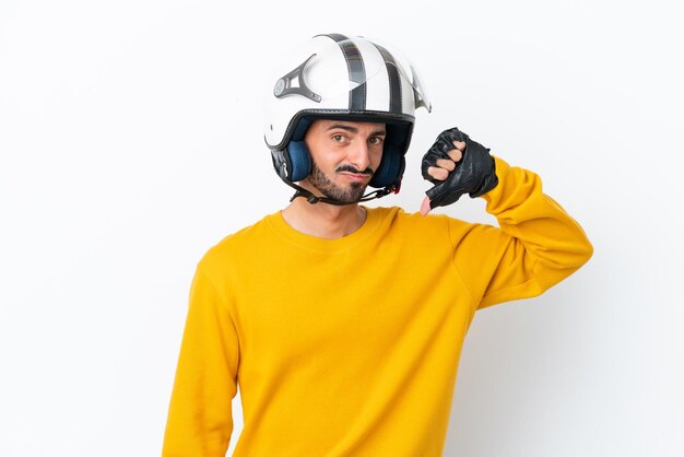 Jovem homem caucasiano com um capacete de moto isolado no fundo branco, mostrando o polegar para baixo com expressão negativa